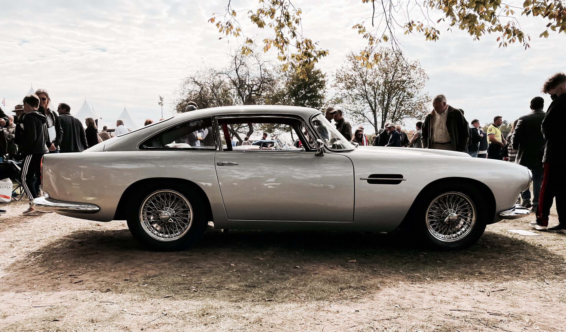 Silver Aston Martin DB4 at a concours lawn event, side profile with wire wheels