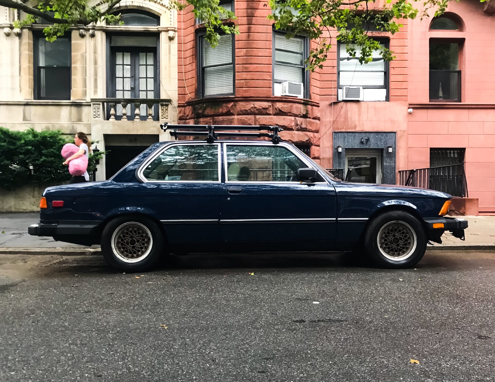 Dark blue BMW 320i with roof rack, side profile in front of a brownstone