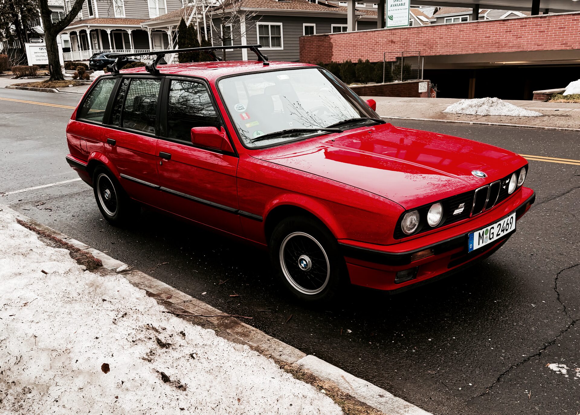 Red BMW E30 Touring wagon with roof rack, parked at the curb