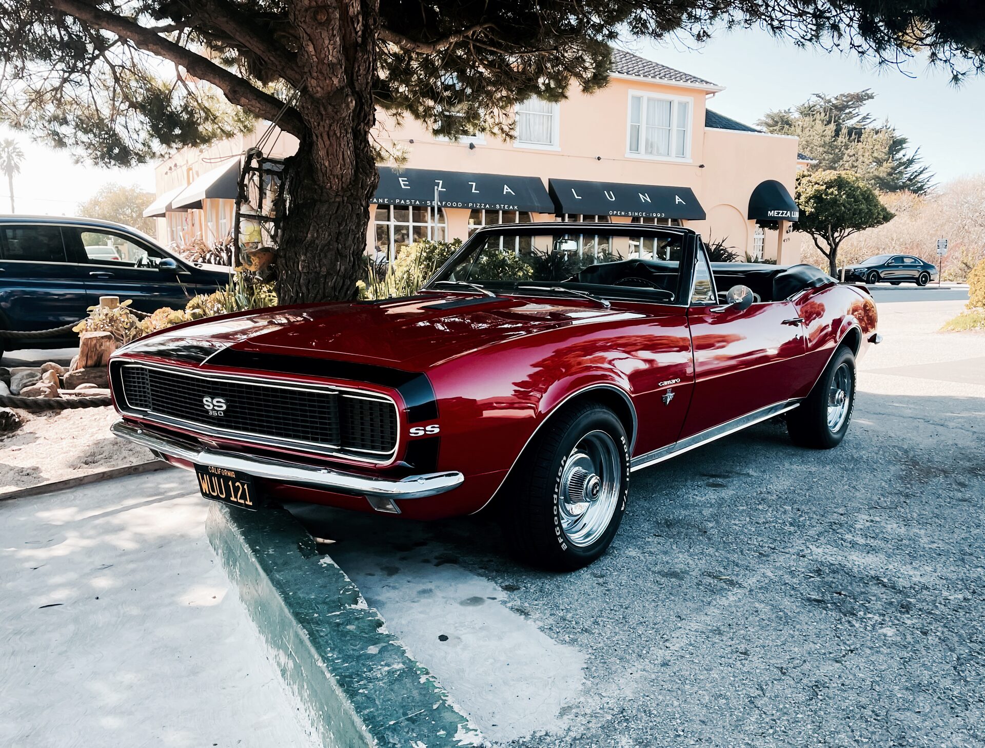 Burgundy 1968 Chevrolet Camaro SS Convertible with top down, parked outside a coastal restaurant