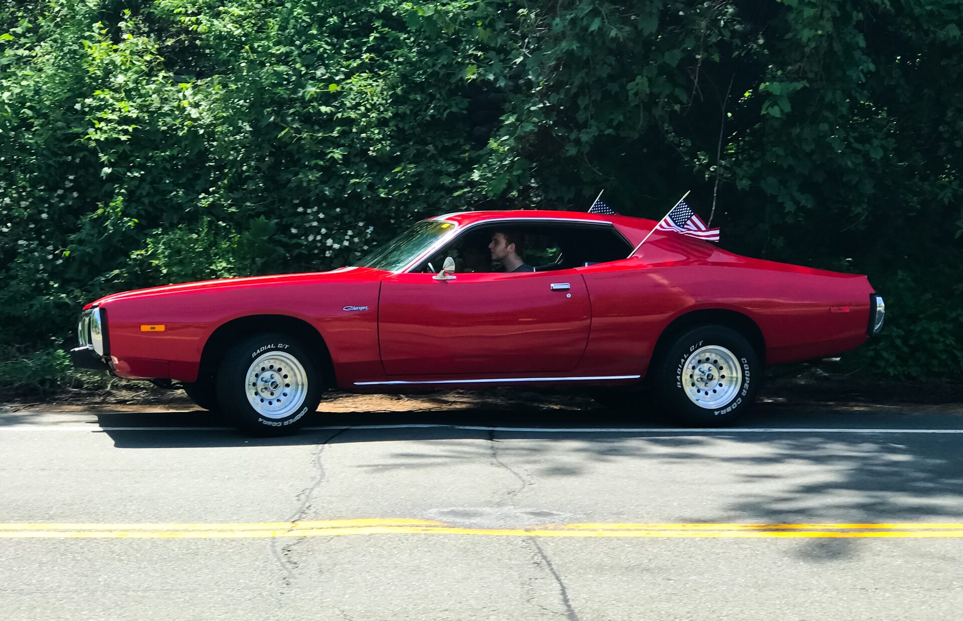 Red Dodge Charger driving on a tree-lined road