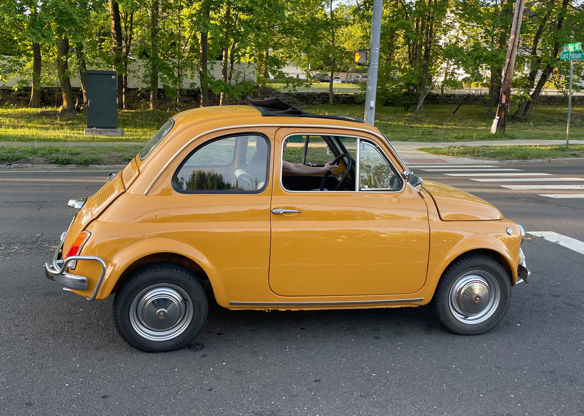 Yellow Fiat 500 with sunroof open, side profile on a leafy suburban road