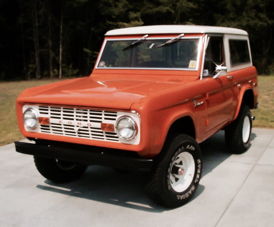 Burnt-orange first-generation Ford Bronco with white roof, parked on a paved drive
