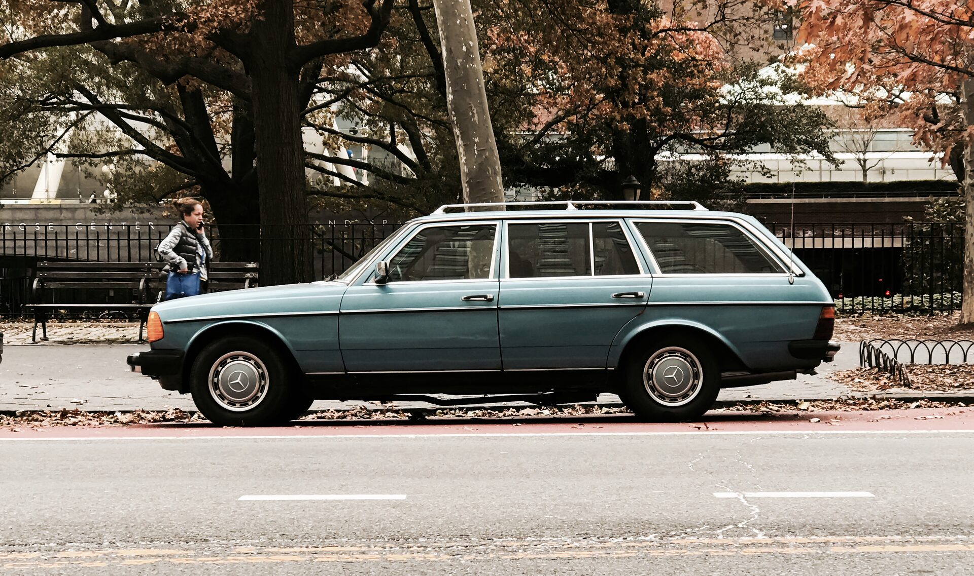 Teal-blue Mercedes-Benz 300TD wagon with roof rack, side profile beside Central Park
