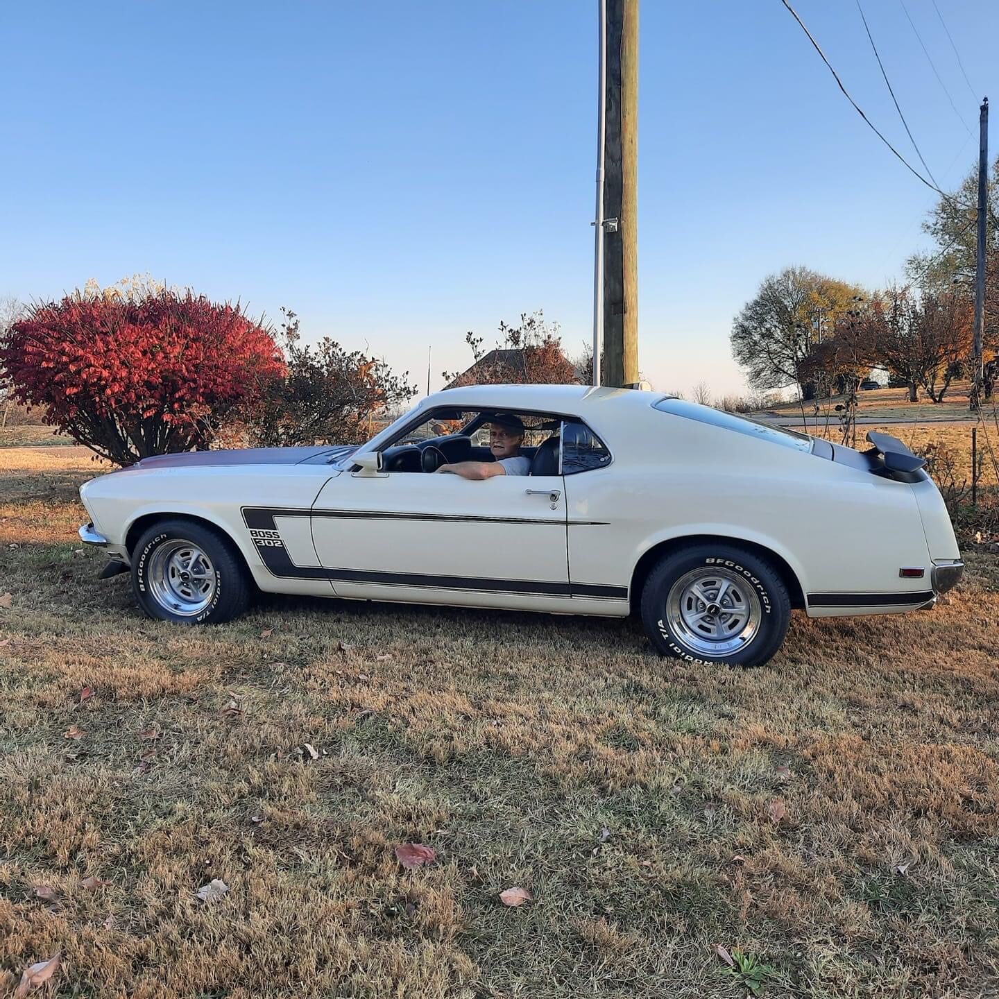 White Ford Mustang Boss 302 with black side stripes, side profile in a rural field