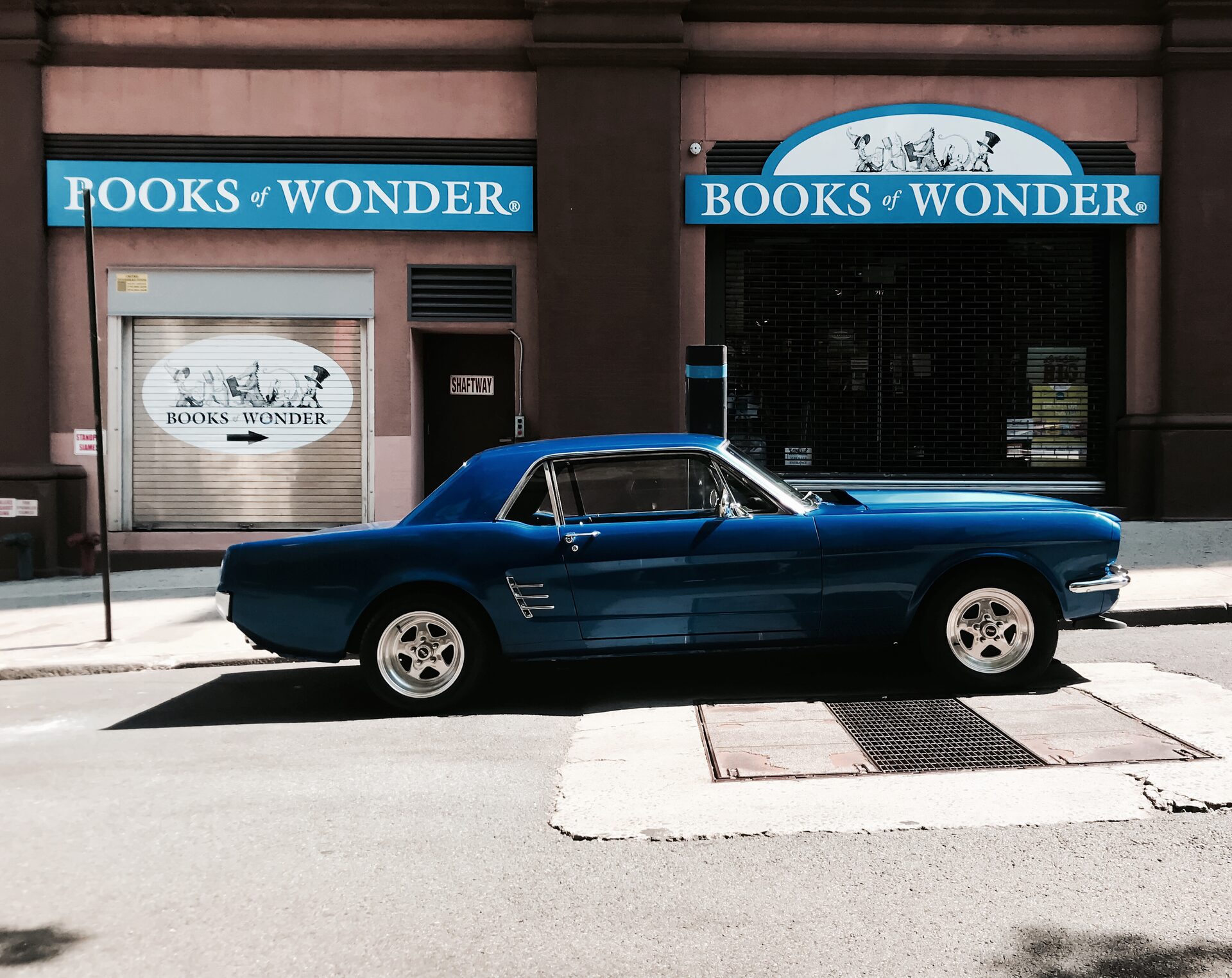 Blue 1966 Ford Mustang coupe, side profile parked outside a Manhattan storefront