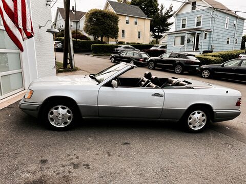 Silver 1995 Mercedes-Benz E320 Cabriolet, side profile with the top down, parked at a residential curb