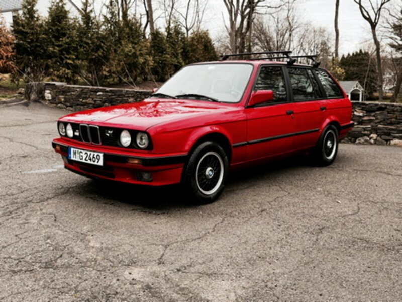 1993 BMW 316i Touring (E30 wagon) in red with roof rack and German plates, parked on a stone-walled driveway